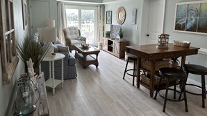 Un salón espacioso con un ventanal grande, un ventilador de techo y una zona de comedor con mesa y sillas de madera.