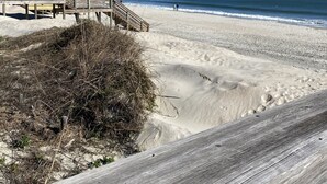 Un paseo marítimo de madera que conduce a una playa arenosa bajo un cielo azul y despejado.