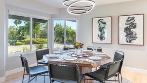 Een eetruimte met een ronde tafel voor zes personen, omringd door zwarte stoelen, met uitzicht op groen.