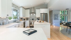 Een moderne keuken met witte kasten, een centraal eiland en een eetgedeelte met uitzicht op de omgeving.