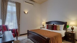 Hotellihuone, jossa on suuri sänky, työpöytä, tuoli ja ikkuna, jossa on verhot.