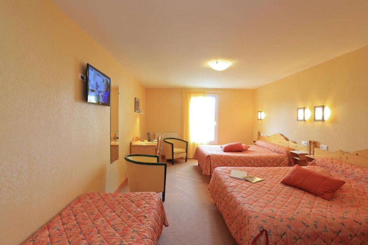 A hotel room with three beds, a desk, a chair, and a television on the wall.