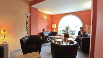 A modern lounge area with leather sofas, wooden tables, and a large window providing natural light.