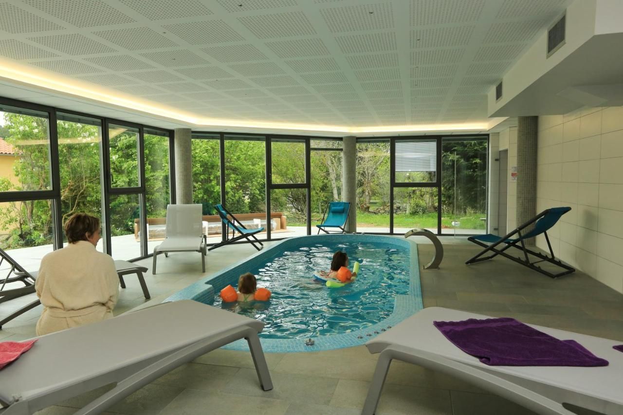 An indoor swimming pool with clear glass walls, lounge chairs, and a ceiling with a grid pattern.