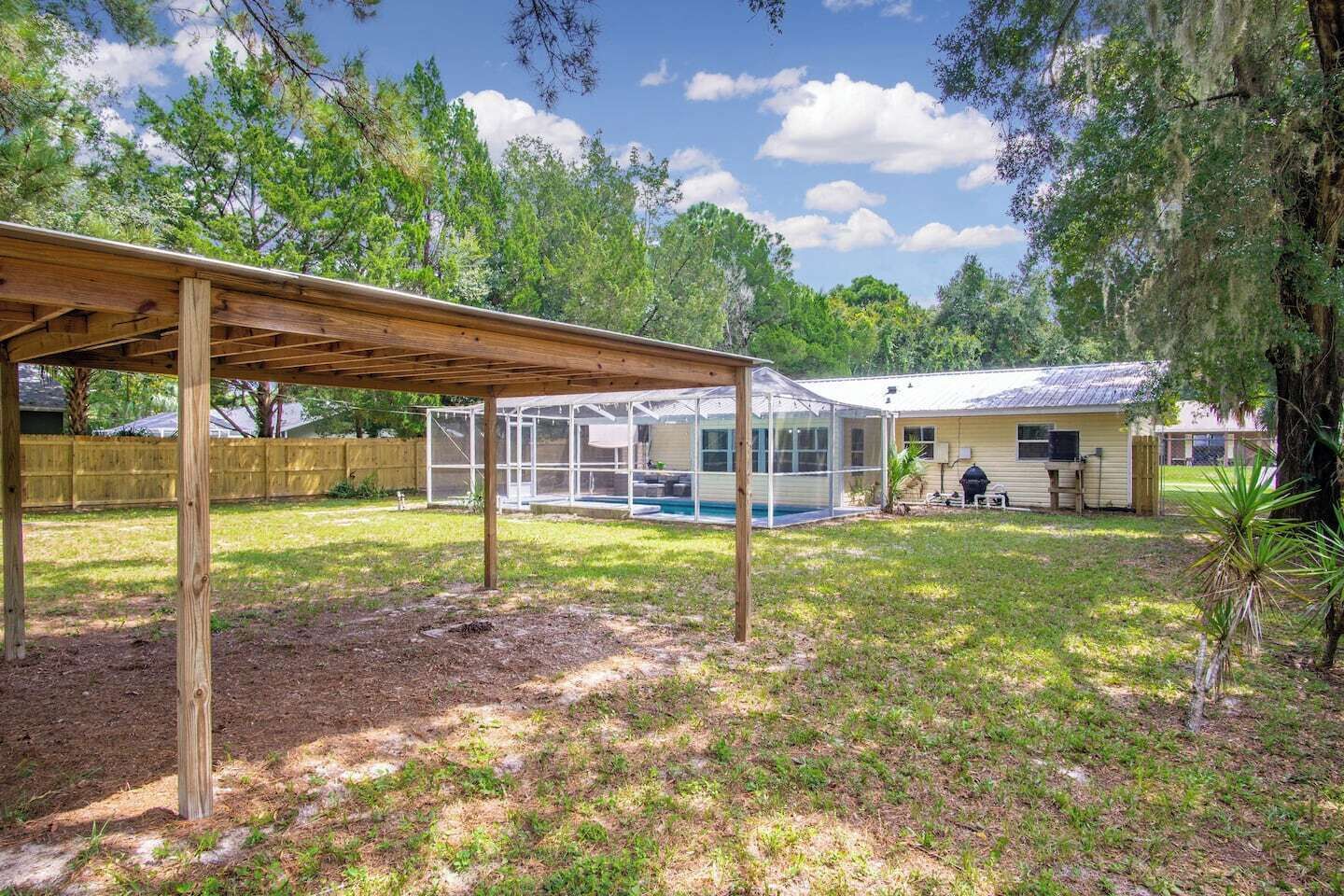 A covered patio area with a pool, a screened-in room, and a house with a barbecue area.