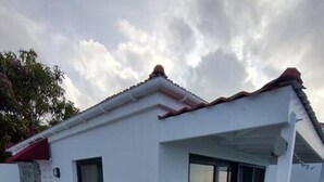 Een klein, wit gebouw met een betegeld terras, een rood dak en een glazen deur.