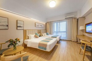 A hotel room with two beds, a desk, a chair, and a TV.