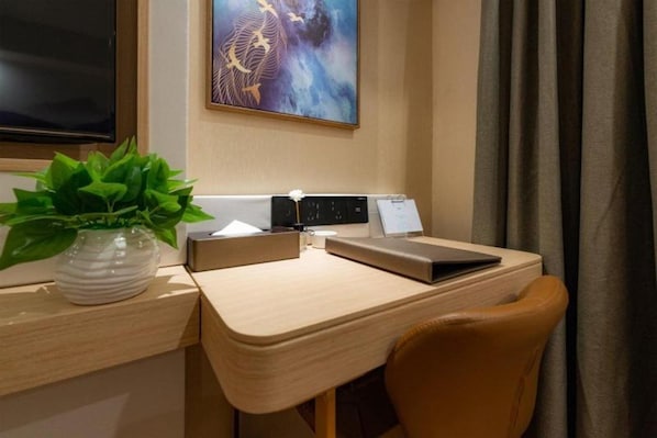 Une chambre d’hôtel avec un bureau, un ordinateur portable, une plante, un tableau et un rideau.