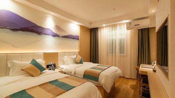Ein Hotelzimmer mit zwei Betten, einem Schreibtisch und einem großen Fenster mit Vorhängen.