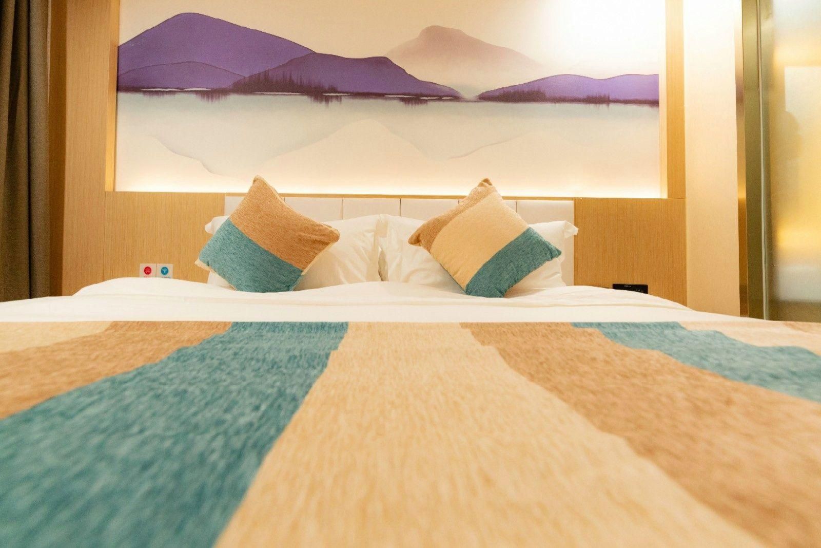 Habitació d'hotel amb un llit, almoines, una manta i un quadre a la paret.