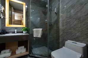 Une salle de bain moderne avec une douche à parois de verre, un mur recouvert de carreaux de marbre, des toilettes blanches et un miroir doté d’un cadre éclairé.
