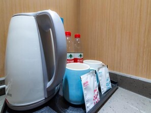 A kettle, two bottles, a mug, and two packets on a tray.