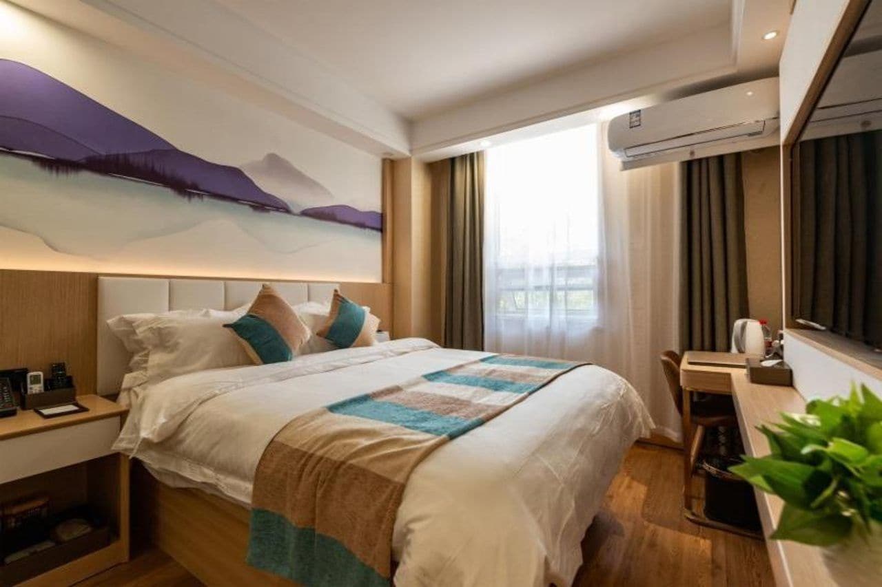 A hotel room with a bed, bedside table, and a window with curtains.