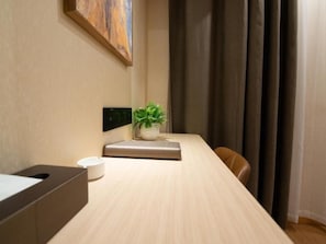 Une pièce avec une longue table en bois, une plante en pot, un objet blanc posé sur la table et une chaise marron.