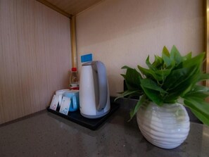 Un plan de travail sur lequel on aperçoit une bouilloire blanche, une bouteille d’eau, une tasse bleue et une plante en pot.