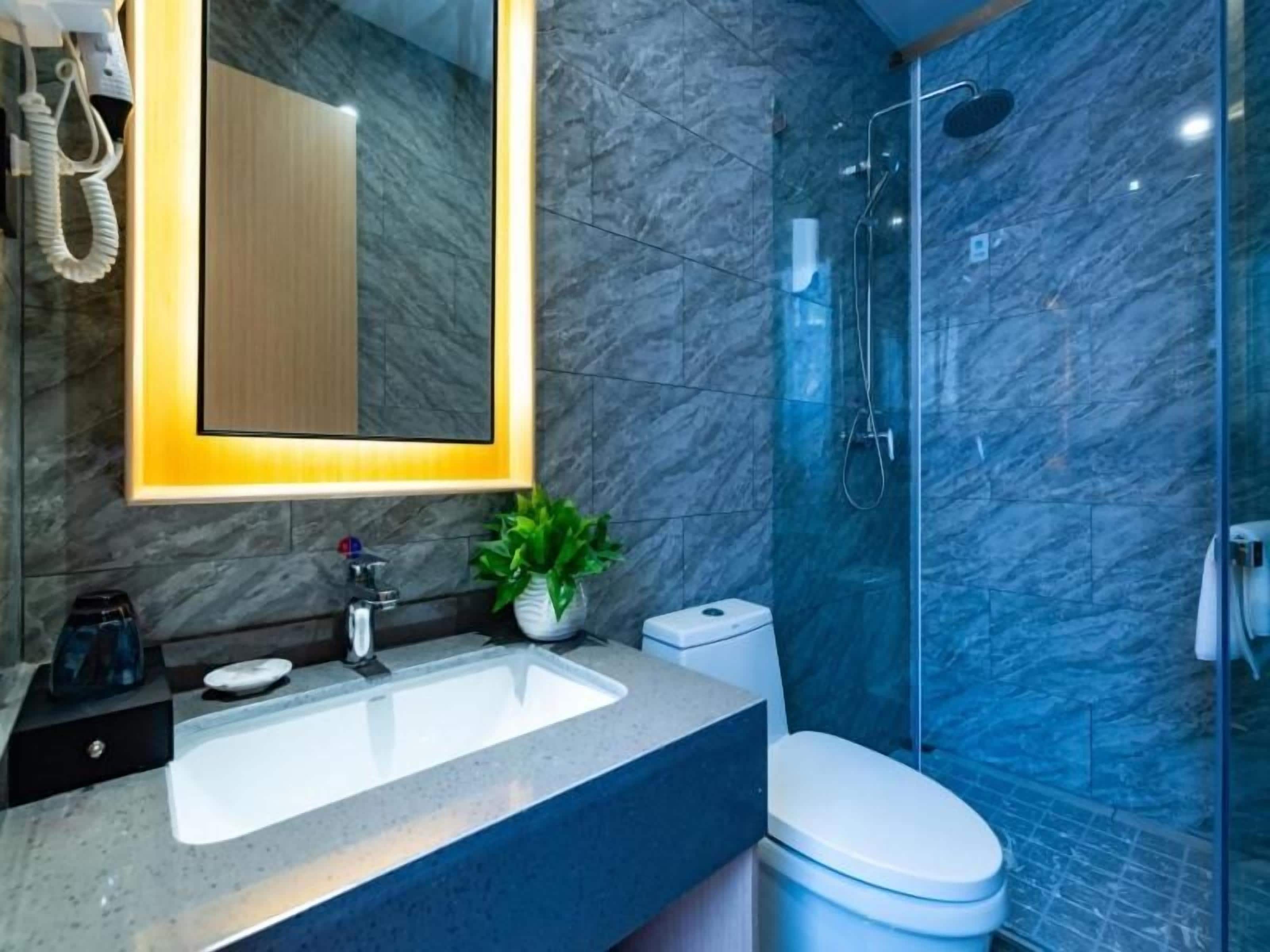 A modern bathroom with a marble sink, a toilet, and a glass-enclosed shower.