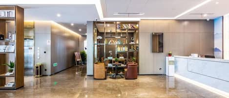A hotel lobby with a reception desk, a seating area with a table and chairs, and a bookshelf filled with books.