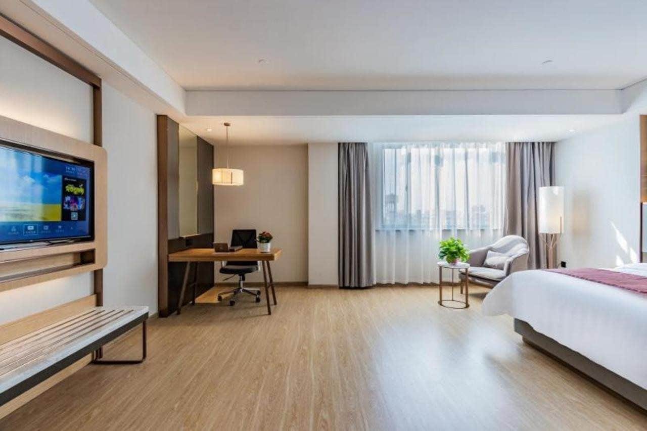 Quarto de hotel com cama, escrivaninha com computador, televisão e janela com cortinas.