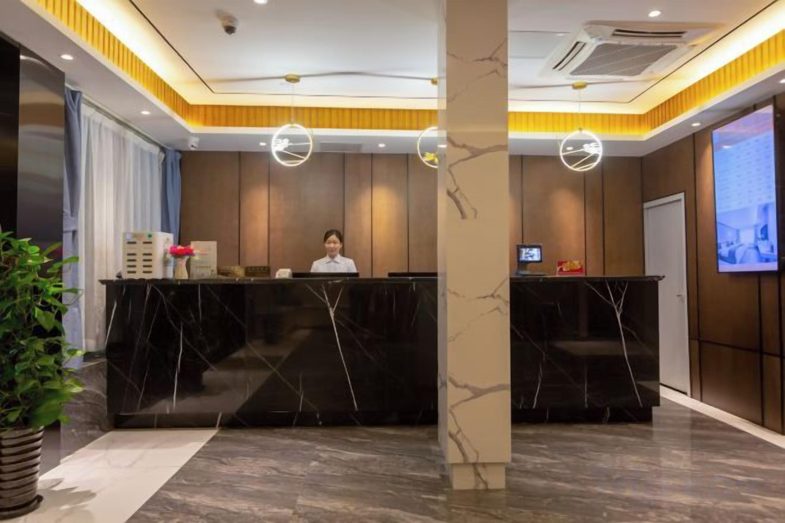 Mostrador de recepción con una recepcionista, una pantalla digital y una pantalla grande que muestra un paisaje urbano.