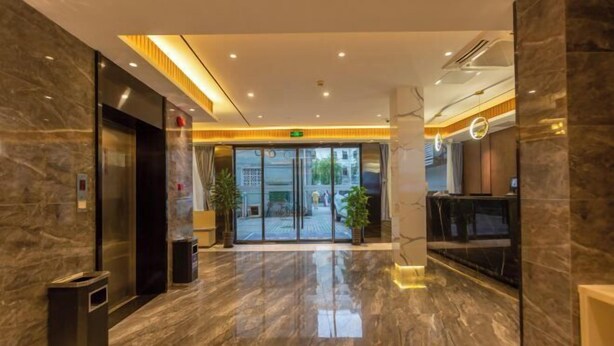 En moderne hotellobby med et marmorgulv, glasdøre der fører udendørs og en receptionsdisk.
