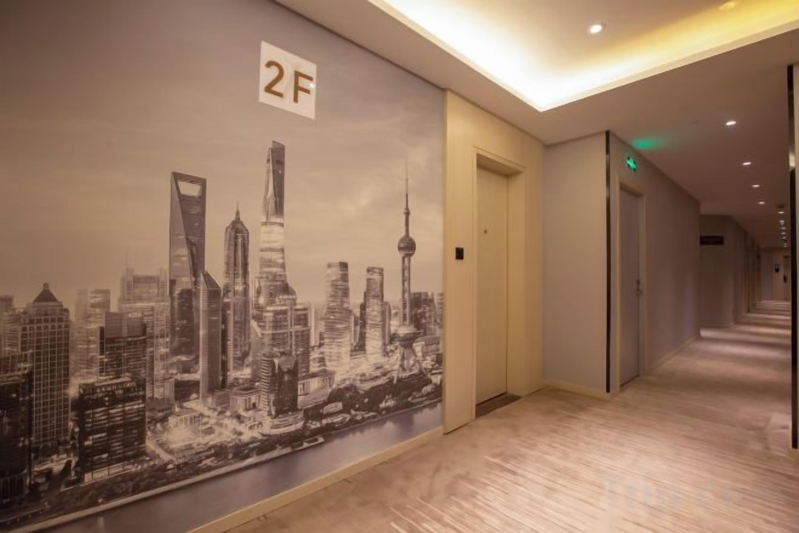 A hotel corridor with a cityscape mural, a door labeled '2F', and a carpeted floor.