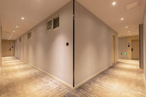 A hotel corridor with a carpeted floor, a door on the right, and a light switch on the wall. - GYA Hotel (Shanghai Railway Station) (Shanghai)