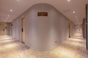 A hotel corridor with a curved wall, a reception area, and a sign with a phone number. - GYA Hotel (Shanghai Railway Station) (Shanghai)