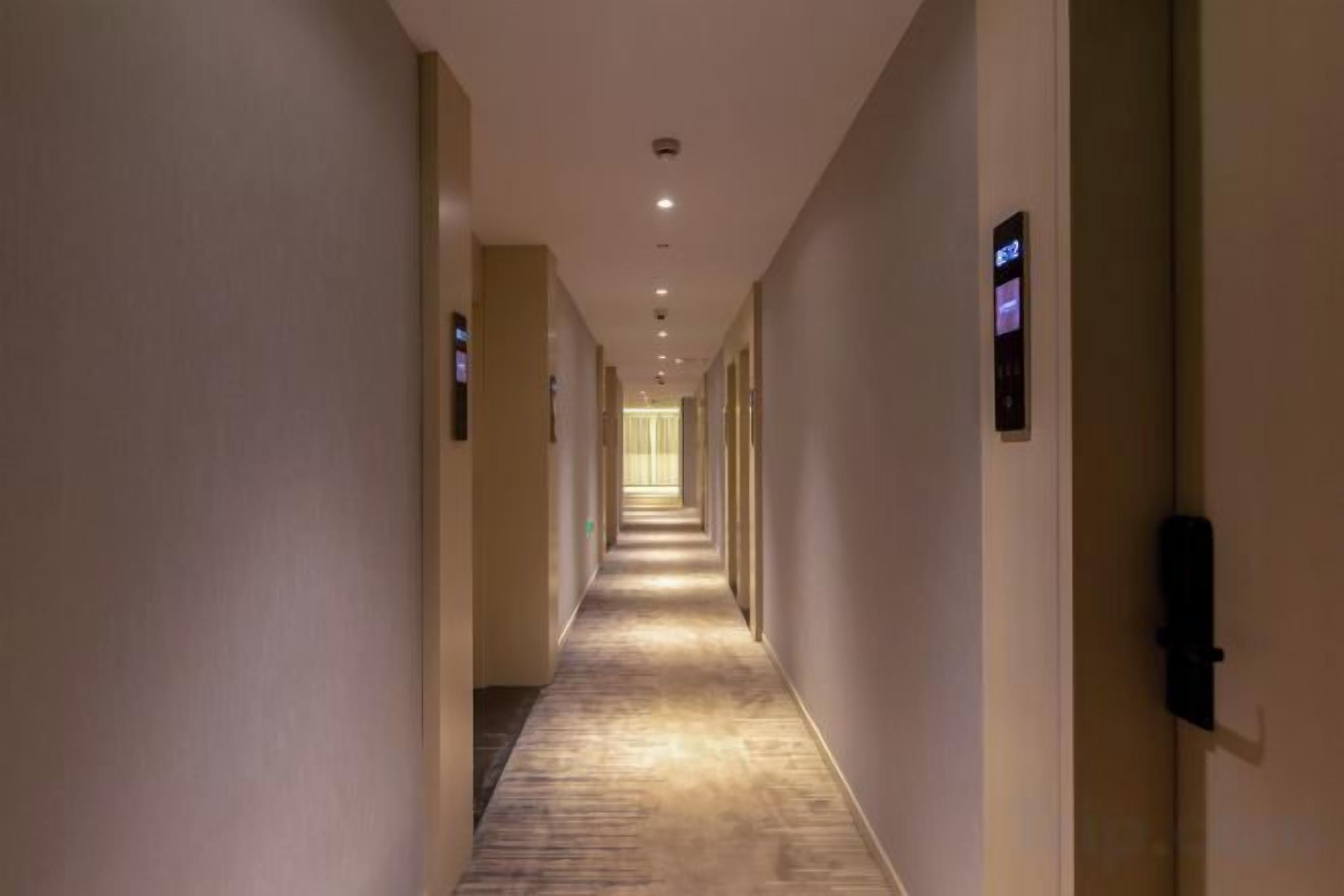 A long, narrow hotel corridor with doors on both sides, leading to individual rooms.
