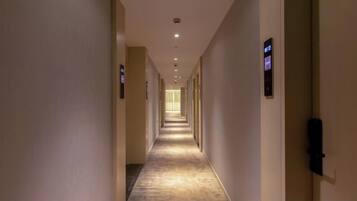 A long, narrow hotel corridor with doors on both sides, leading to individual rooms.