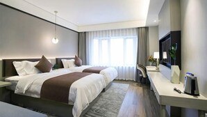 Et moderne hotelværelse med to senge, et skrivebord, et fjernsyn og et stort vindue.