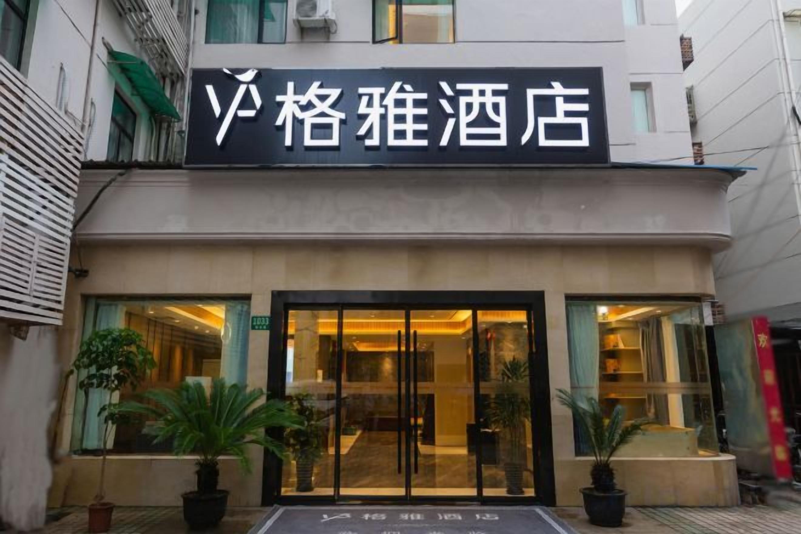A hotel entrance with a sign, potted plants, and a glass door.