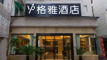 A hotel entrance with a sign, potted plants, and a glass door.