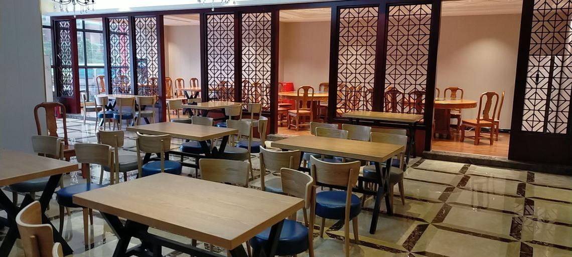 Interior de restaurante con varias mesas y sillas, suelo de madera y paneles decorativos.
