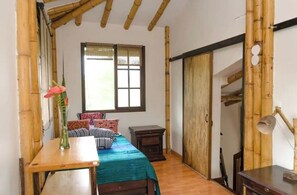 A bedroom with a bed, bedside table, lamp, and a window with bamboo walls.