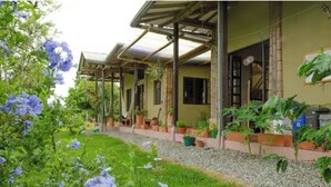A covered outdoor area with a garden path, potted plants, and a building with windows and doors. - Charming coffee region farm escape (Armenia)