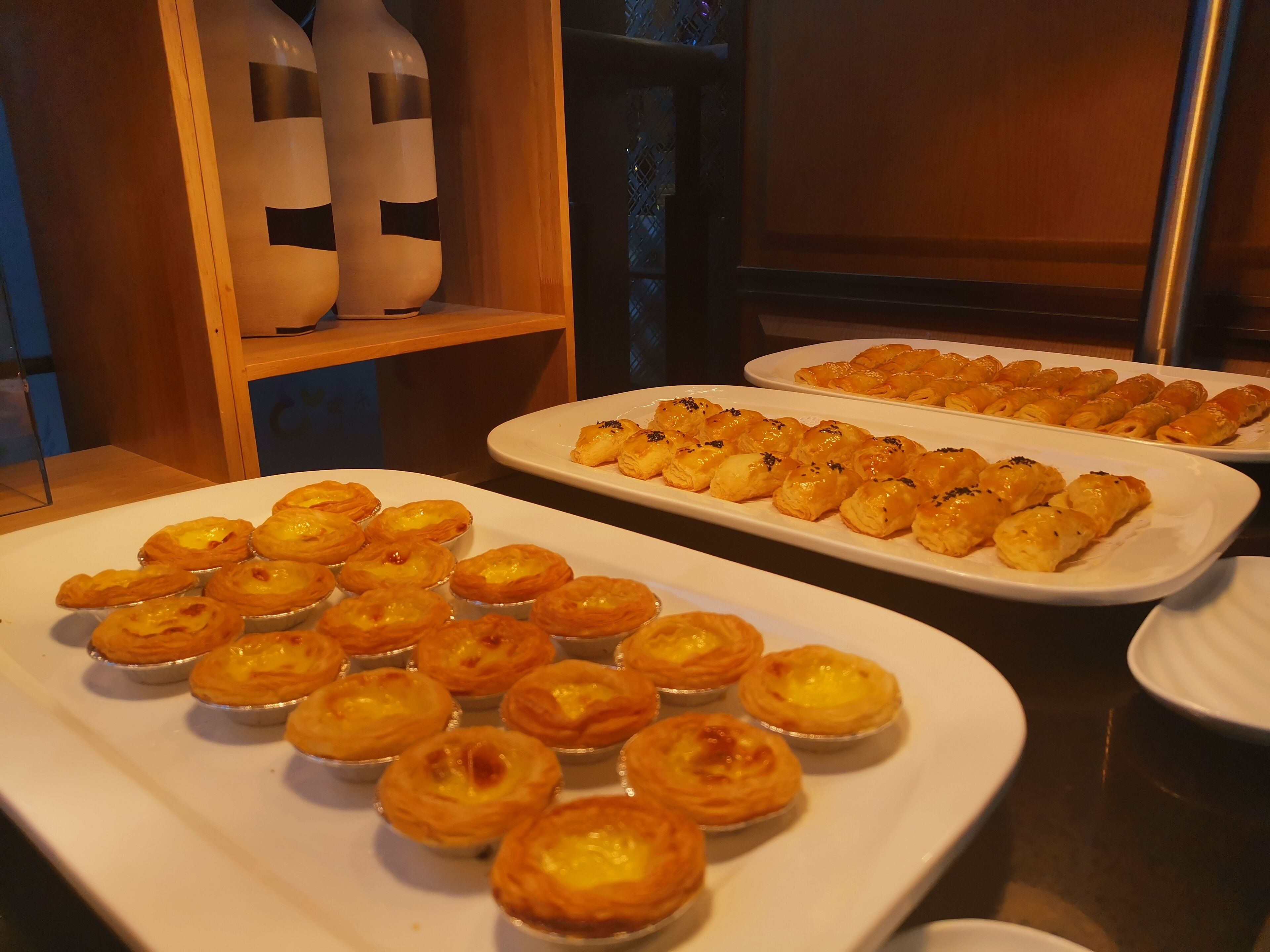 A buffet table with various pastries, including custard tarts and puff pastries, arranged on white plates.