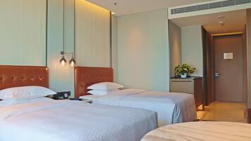 A hotel room with two beds, a headboard, bedside tables, a nightstand, a plant, and a door leading to another room.
