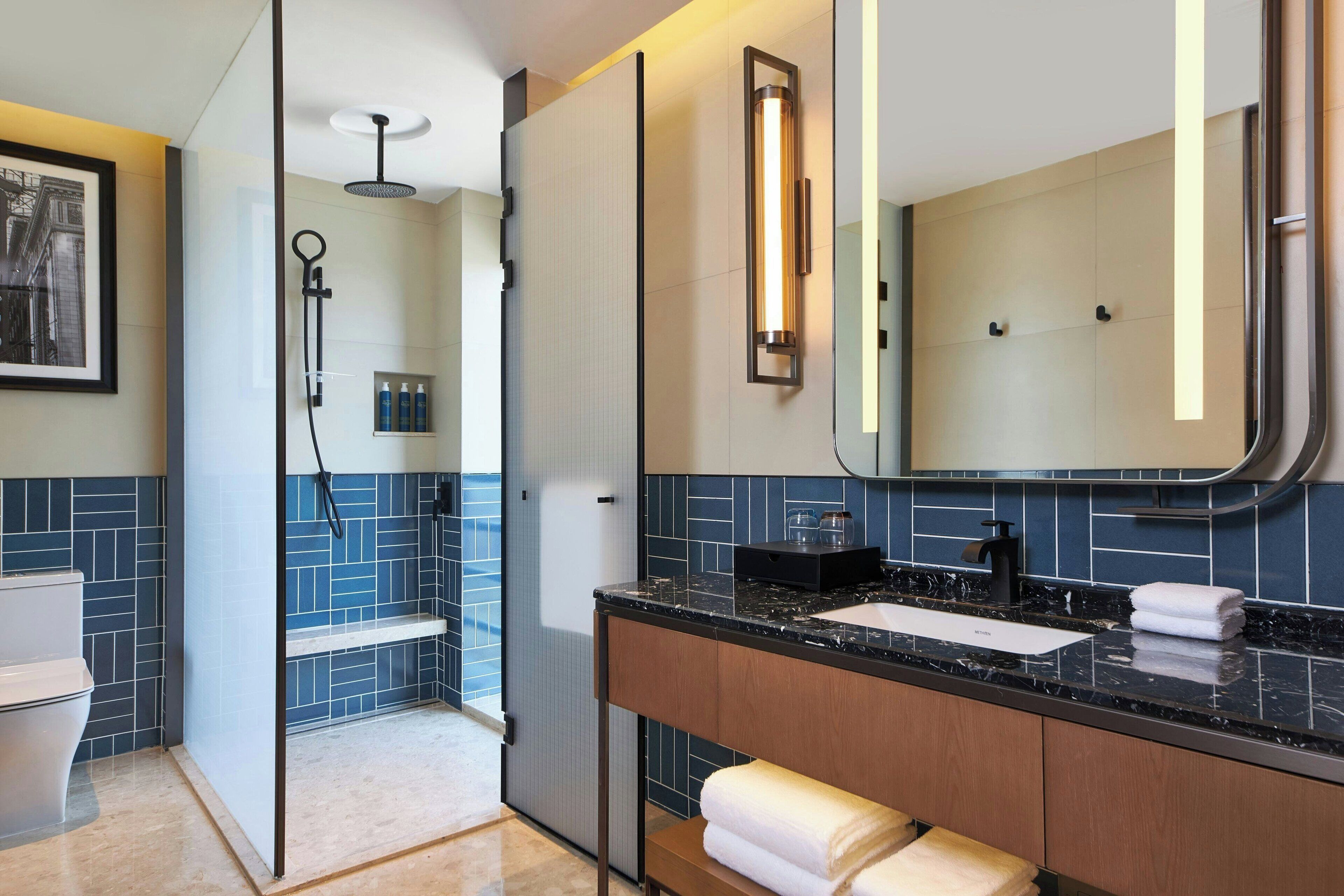 A modern bathroom with a glass shower enclosure, a marble countertop, and a large mirror.