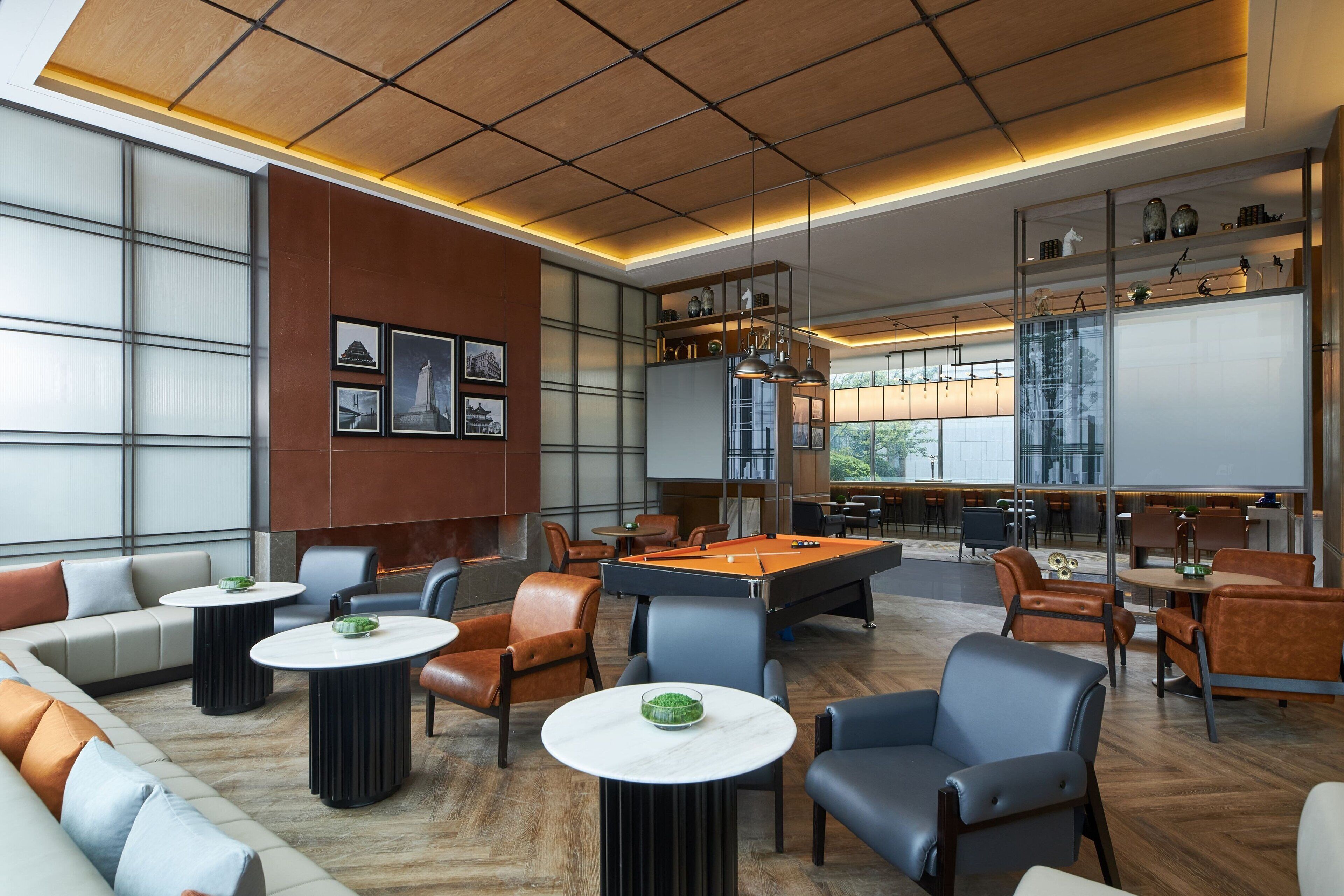 A modern lounge area with a pool table, comfortable seating, and a large window providing natural light.