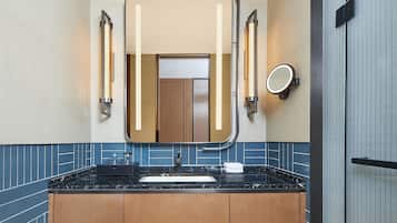 A modern bathroom with a black marble sink, wooden cabinets, and a large mirror with integrated lighting.