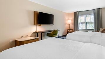 Habitación de hotel con dos camas, un escritorio con silla, televisión montada en la pared y ventana con cortinas.