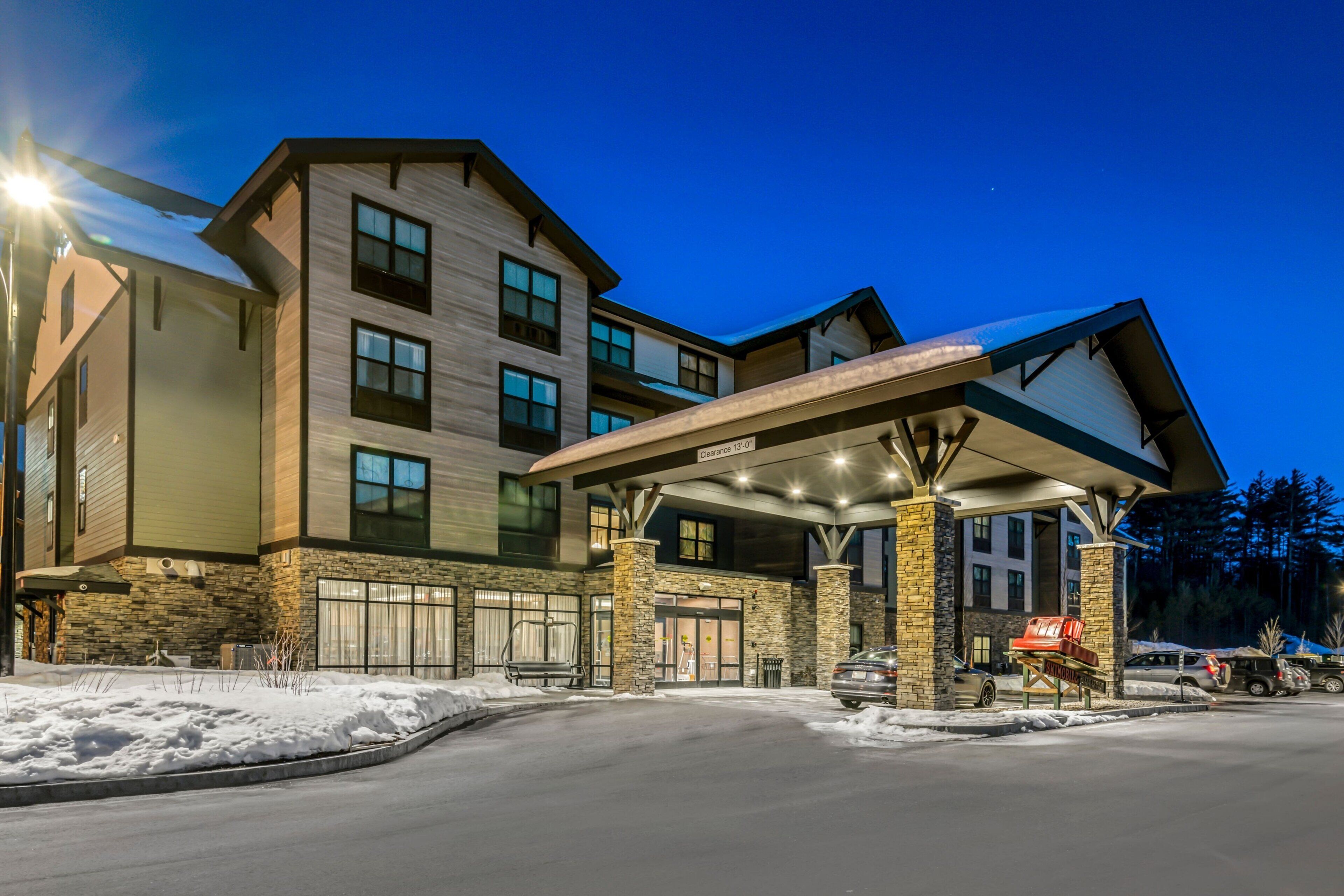 A multi-story hotel with a covered entrance, stone facade, and snow on the ground.