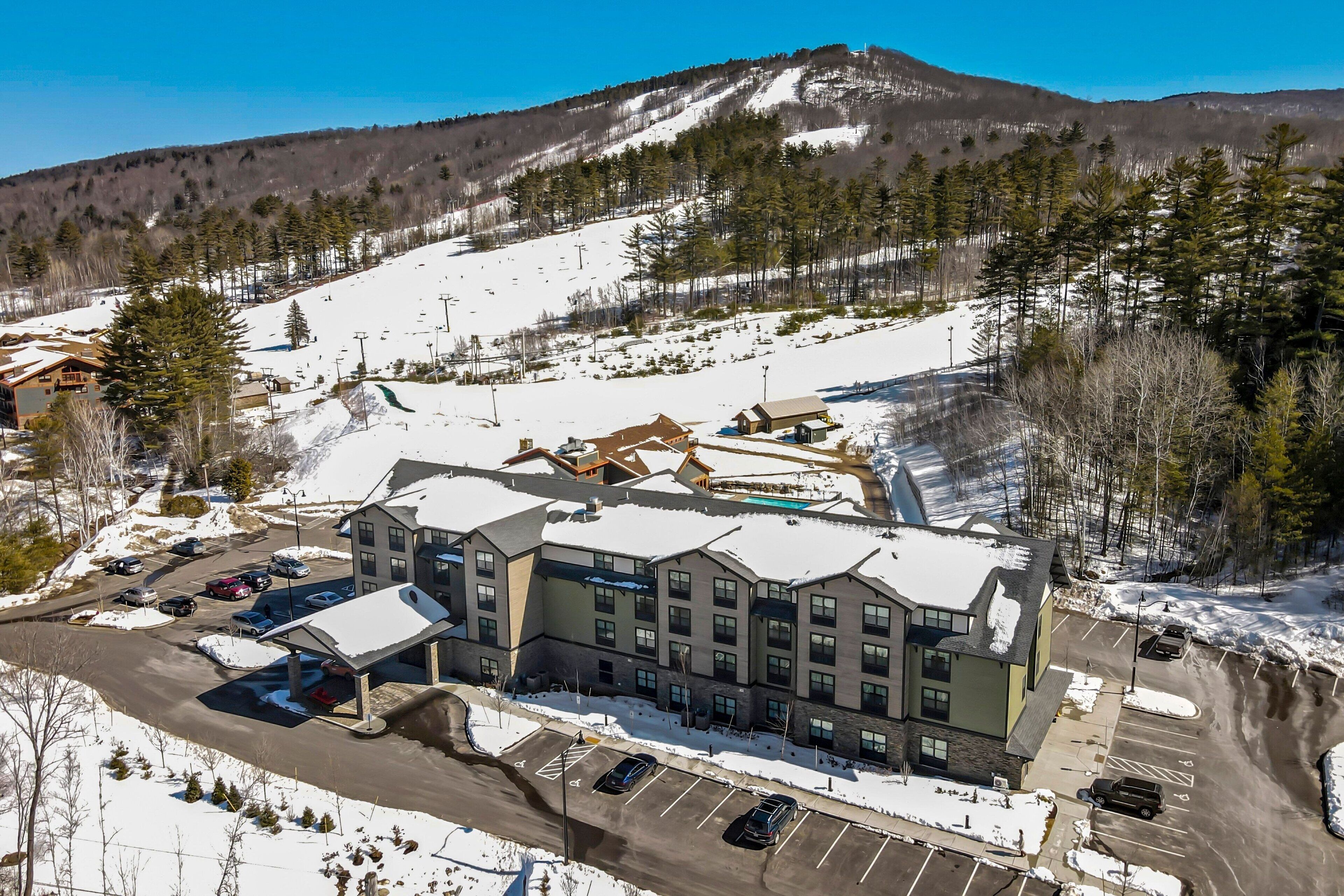 A multi-story hotel with a ski lift in the background, surrounded by snow-covered terrain and trees.