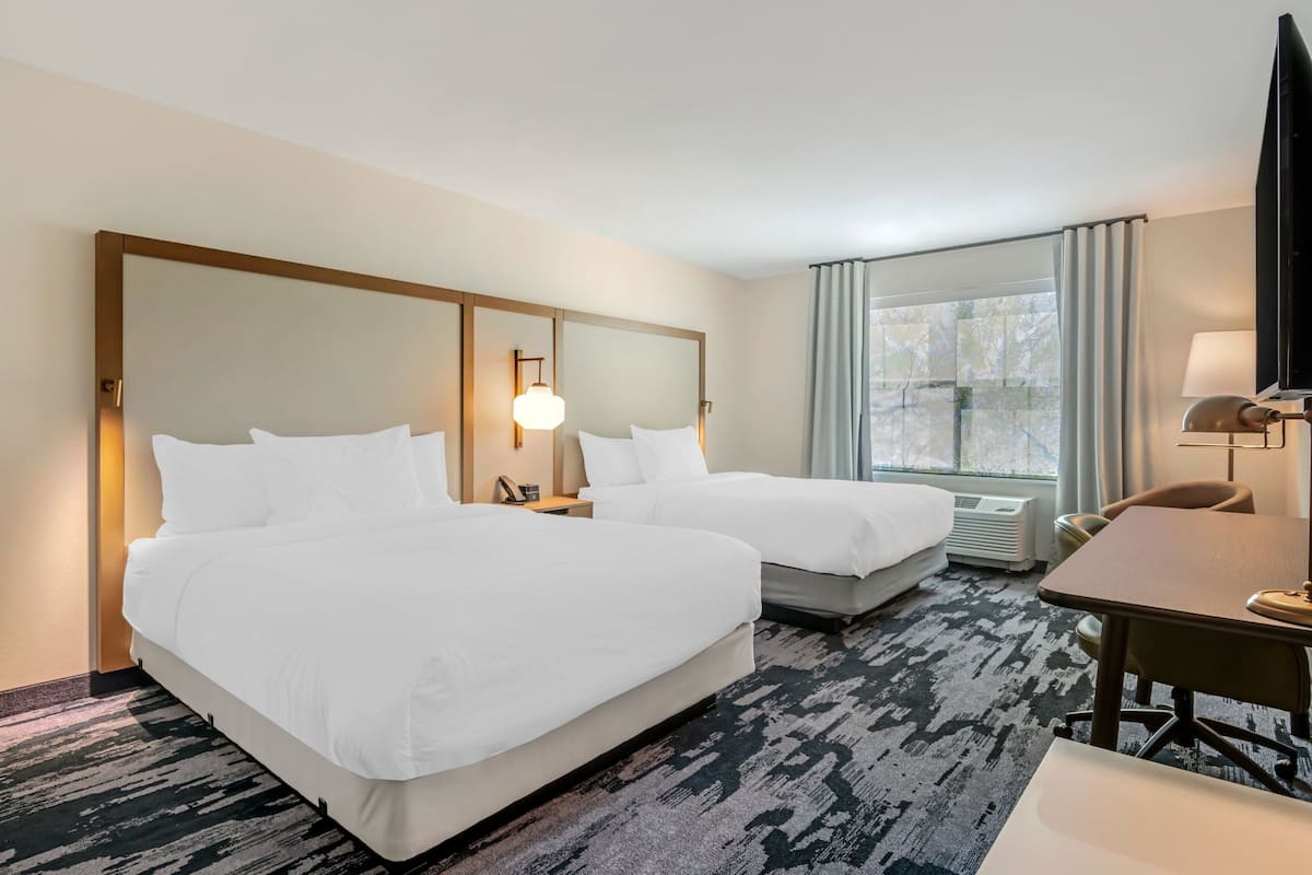Una habitación de hotel con dos camas, un escritorio, una silla, un televisor y una ventana con cortinas.
