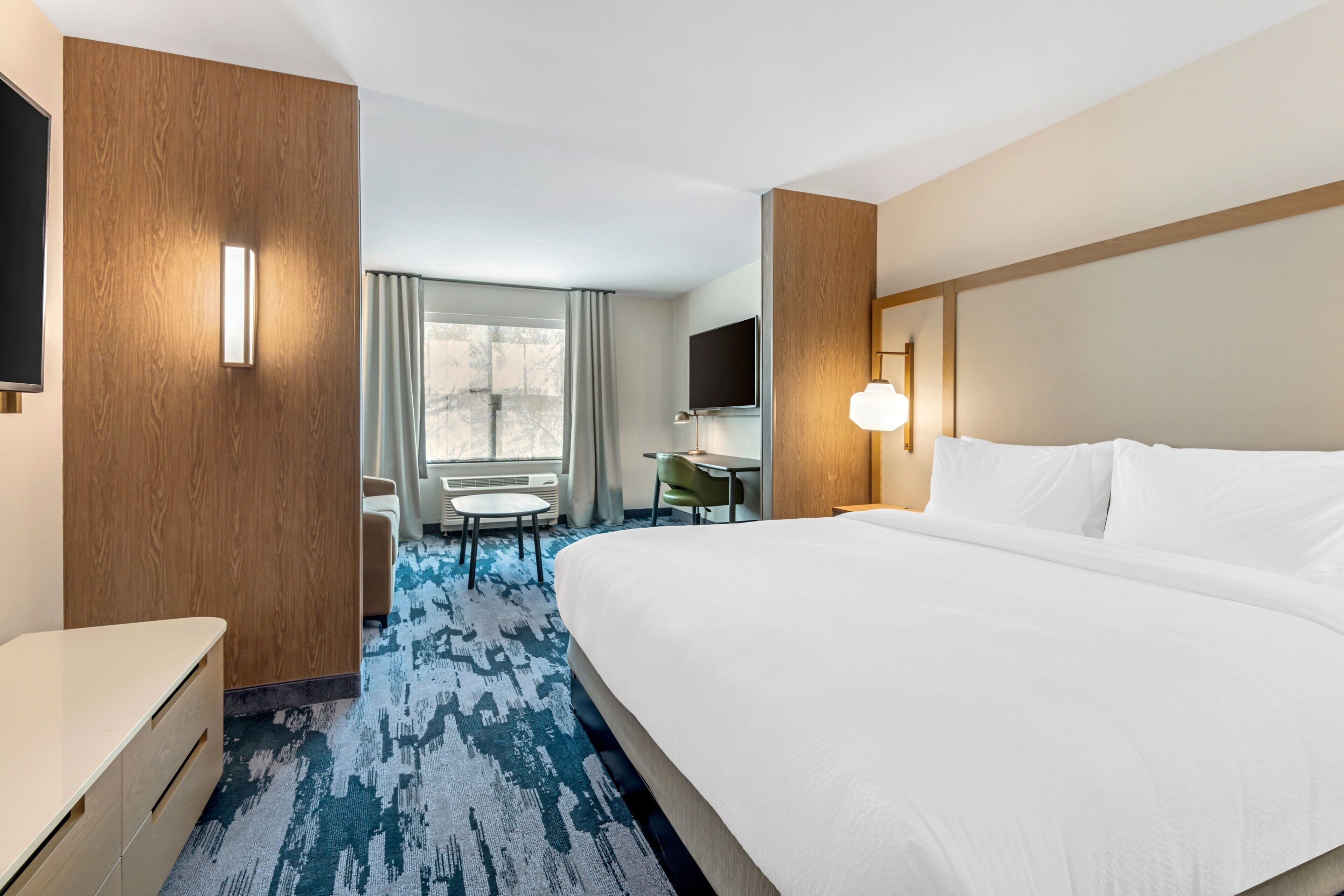 Habitación de hotel con una cama grande, un escritorio, una silla, un televisor y una ventana con cortinas.