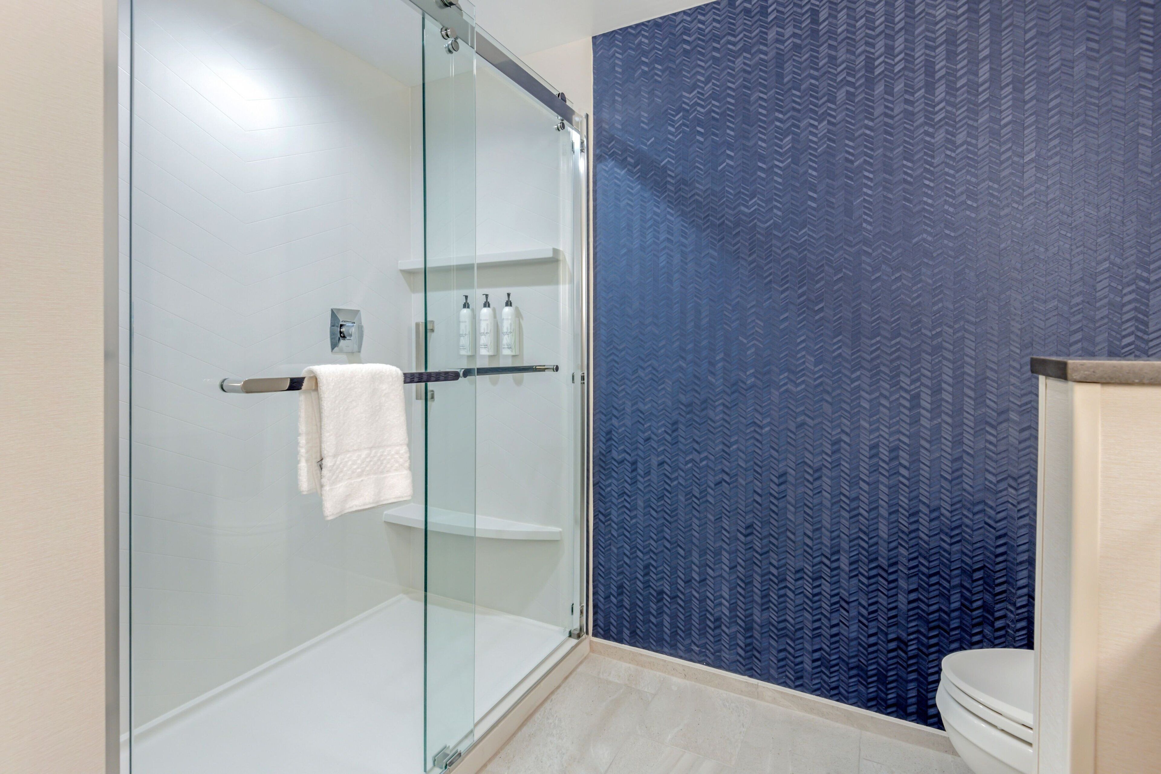 A modern bathroom with a glass shower enclosure, a white toilet, and a blue patterned wall.