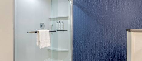 A modern bathroom with a glass shower enclosure, a white toilet, and a blue patterned wall.