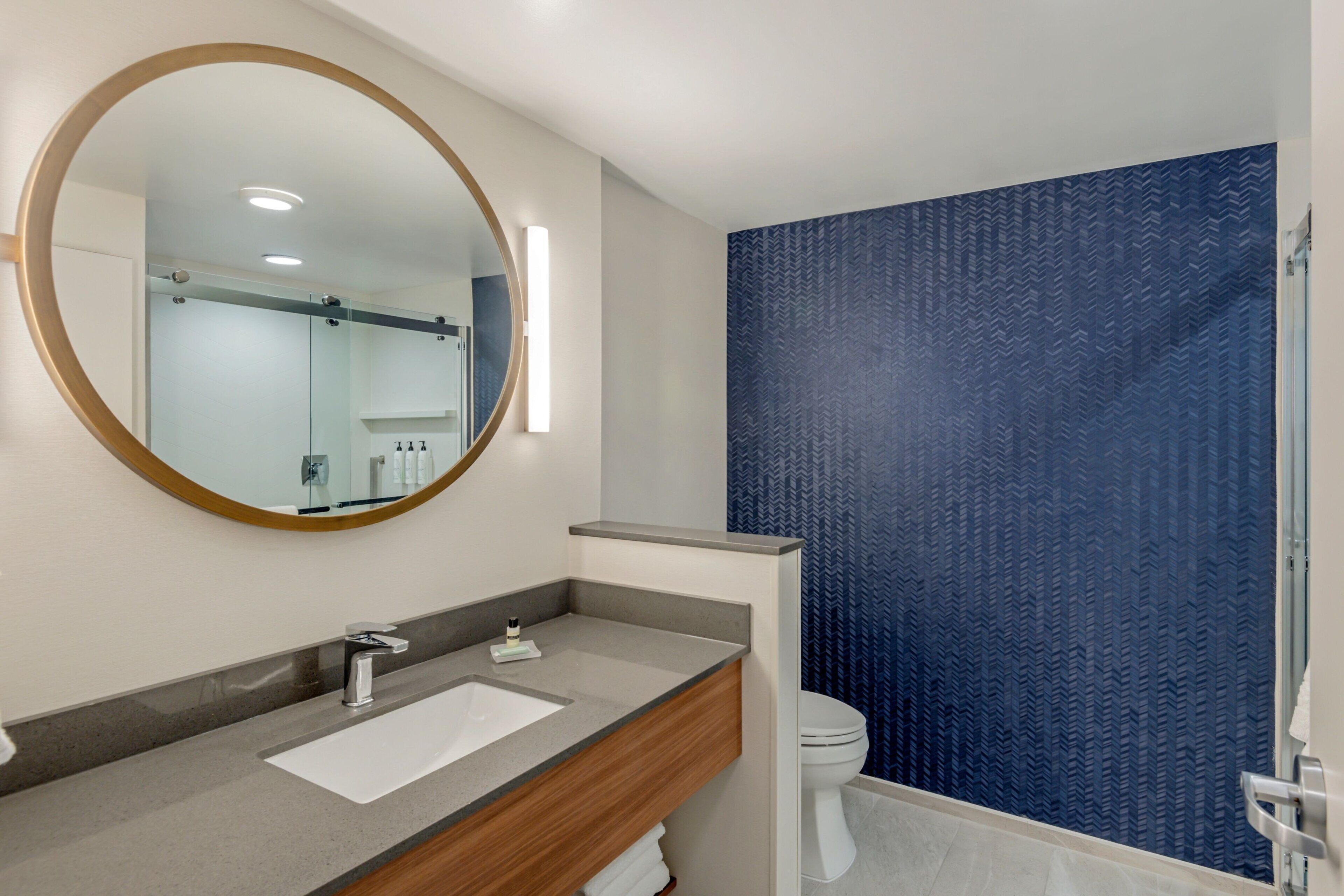Un baño moderno con un espejo redondo, un lavamanos y un inodoro.