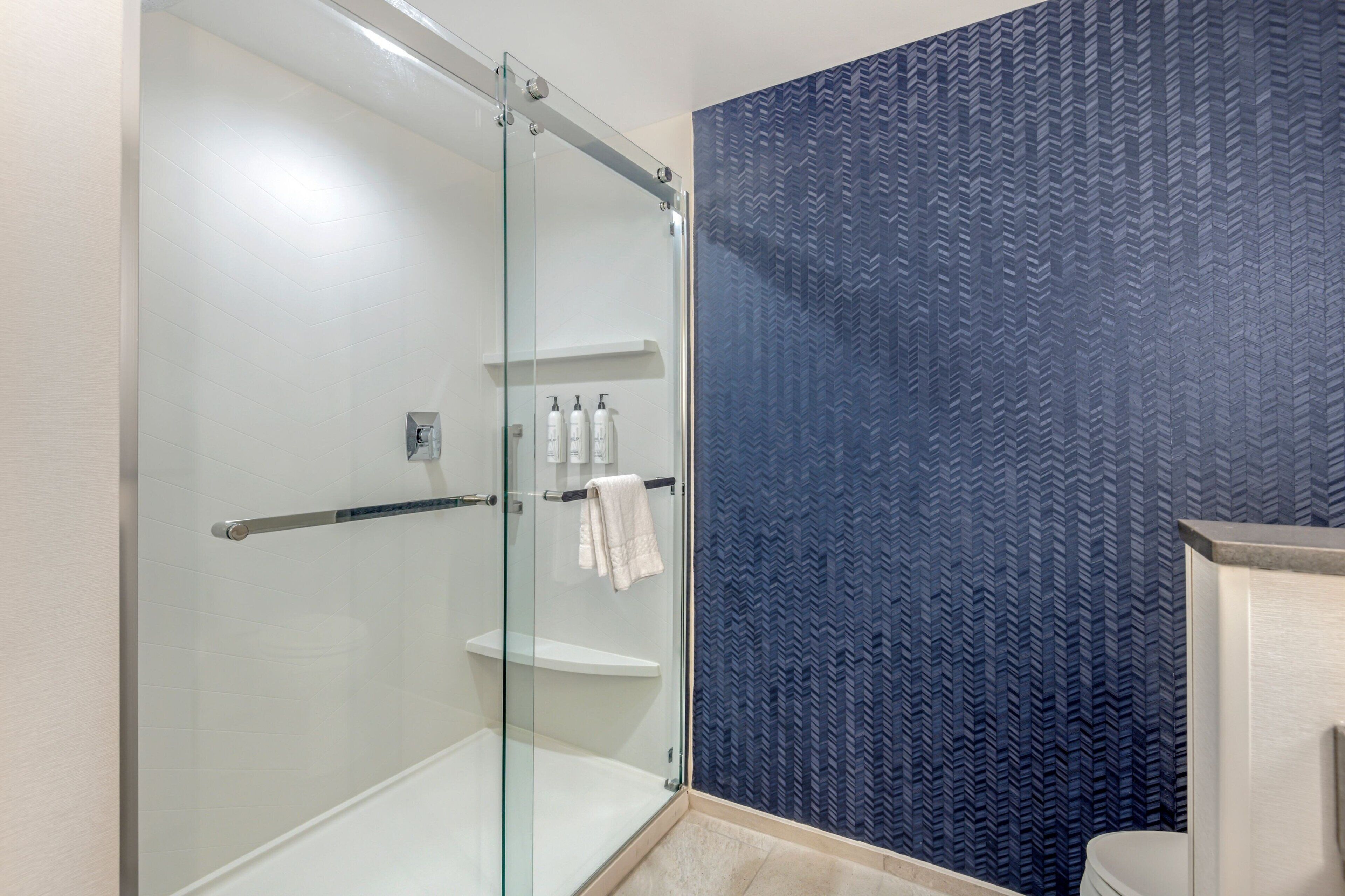 A modern bathroom with a glass-enclosed shower, a blue patterned wall, and a white sink with a towel rack.