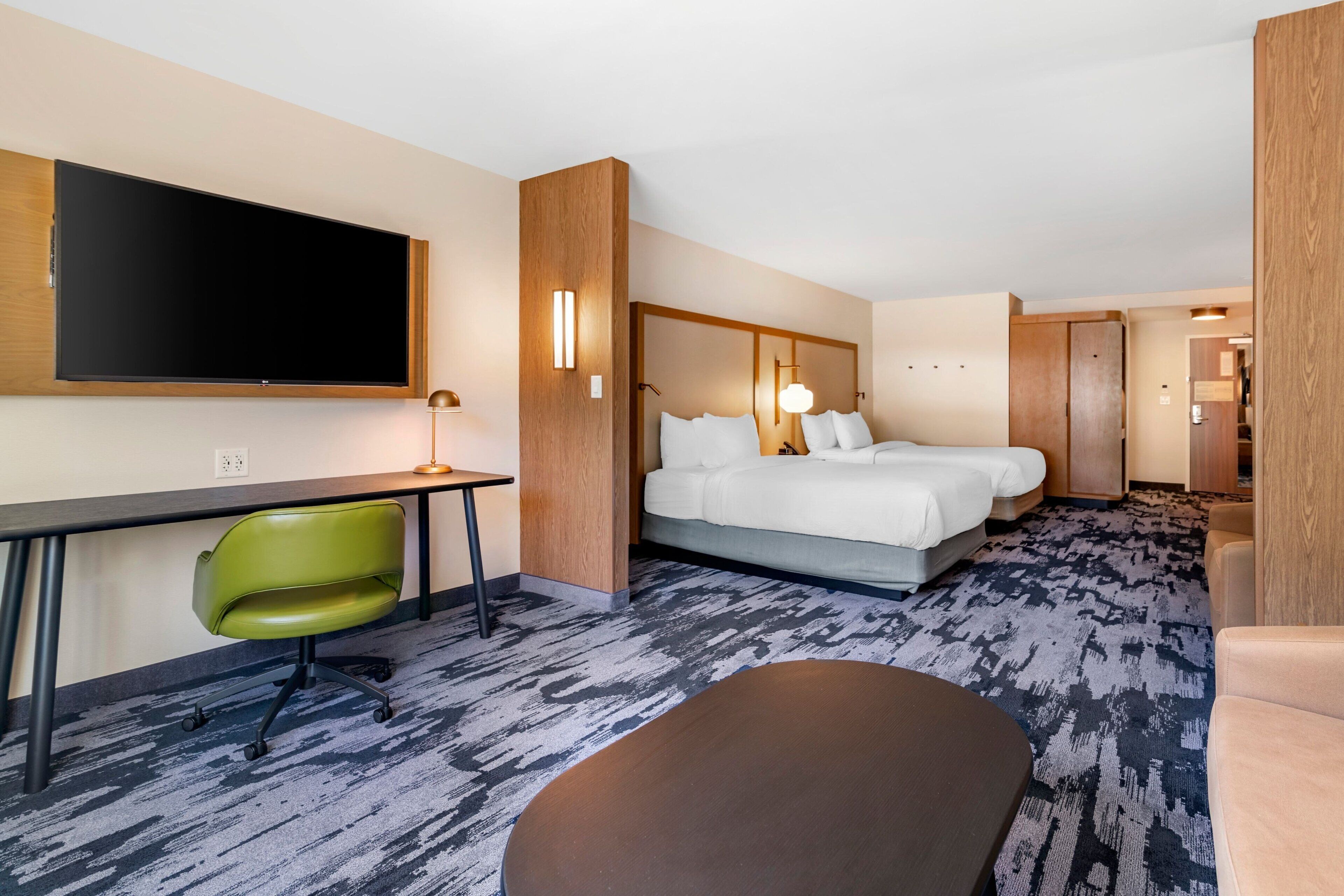A hotel room with a bed, a desk, a chair, and a television.